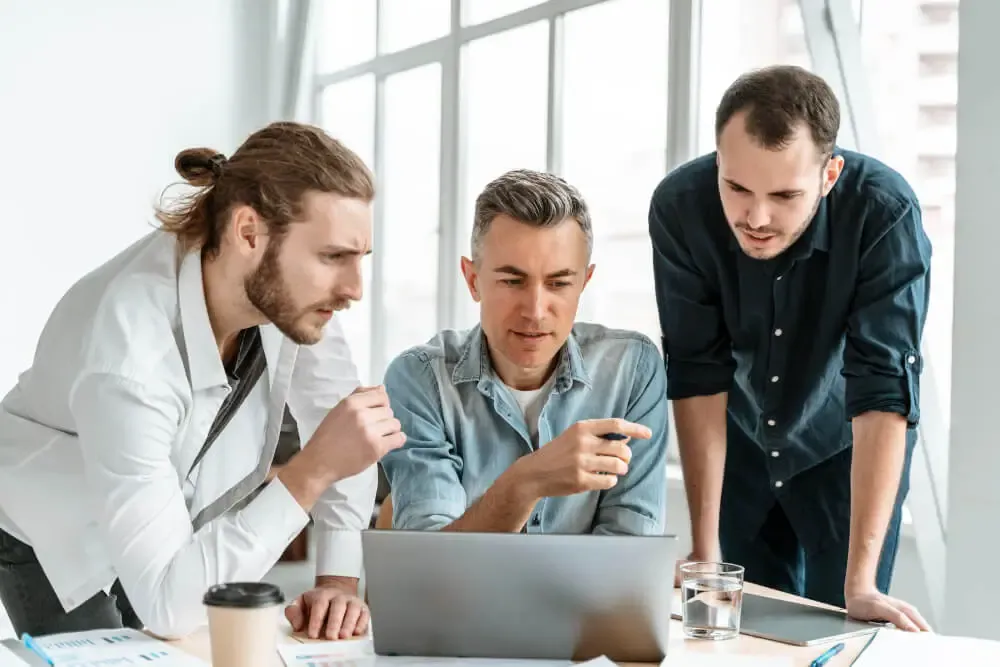 Three colleagues gathered around a laptop.